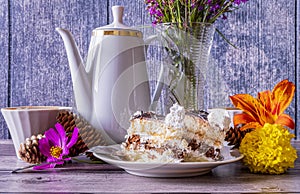 Two pieces of cake in plate, teapot and cups, wild flowers in vase stand on wooden table. Positive mood.