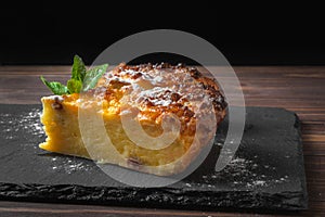 Two pieces of cottage cheese casserole with mint leaves and powdered sugar. On a black slate stand