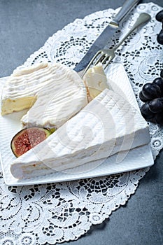 Two pieces of French soft cheeses Brie and Camembert with white mold and strong odor, served with fresh ripe figs and black grapes