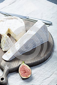 Two pieces of French soft cheeses Brie and Camembert with white mold and strong odor, served with fresh ripe figs