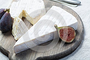 Two pieces of French soft cheeses Brie and Camembert with white mold and strong odor, served with fresh ripe figs
