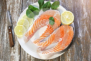 Two pieces of fresh salmon steak on a white plate with spinach and lemon, on  a gray wooden background. Omega 3 vitamin, healthy