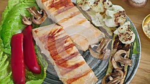 two pieces of fried salmon is placed on a plate with food and adjusted with a fork. mushrooms and red peppers on a plate