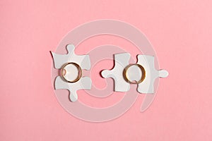 Two pieces of paper jigsaw puzzles with golden wedding rings isolated on pink background, top view