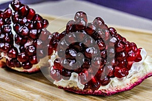 Two pieces of pomegranate with red seeds on a wooden tray. Pomegranate seeds. One piece in front and the other piece of ripe