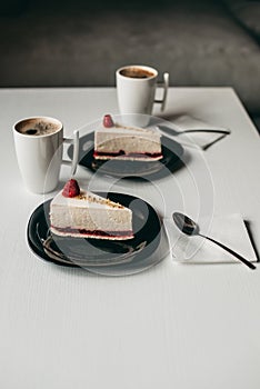 Two pieces of raspberry cheesecake dessert with coffee in a white cup on  table in a cafe