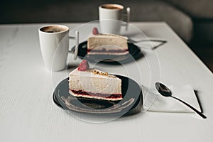 Two pieces of raspberry cheesecake dessert with coffee in a white cup on  table in a cafe