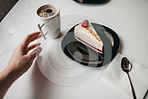 Two pieces of raspberry cheesecake dessert with coffee in a white cup on  table in a cafe