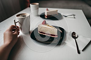 Two pieces of raspberry cheesecake dessert with coffee in a white cup on  table in a cafe