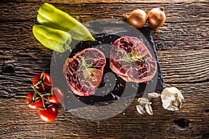 Two pieces raw beef shank and basic ingredients on goulash - onion pepper tomatoes garlic salt spices and rosemary