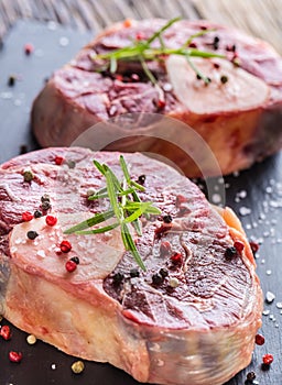 Two pieces raw beef shank on slate board and wooden table.