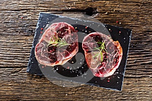 Two pieces raw beef shank on slate board and wooden table.