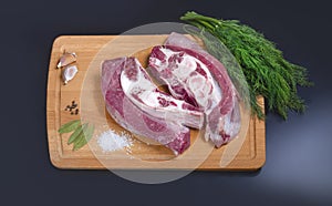 Two pieces of raw beef with spices on a cutting board. Black background