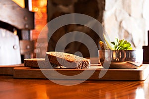 Two pieces of sliced black bread and pickles in a bowl as a snack lie on a wooden board on a table under the sun, bread