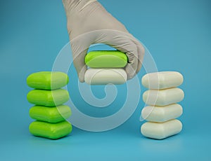 Two pieces of soap in one human hand, protective glove, blue background