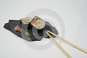 two pieces of sushi in a blackboard plate with chopstick, ginger and wasabi