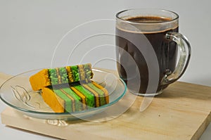 Two pieces of yellow-green lapis legit cake with a glass of coffee