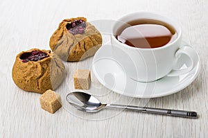 Two pies with lingonberry, tea, sugar cubes, teaspoon on table