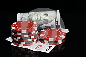 Two piles of poker chips and money are on playing cards on a glossy black background