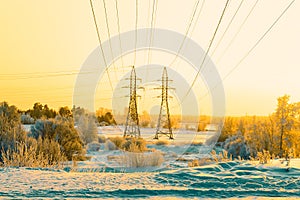 Two pillars of high voltage line and wires through riverplain in winter. Sunset