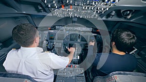 Two pilots landing a plane in a simulator, back view.