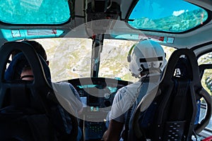 Two pilots seen from behind, flying a helicopter, sitting in a cabin