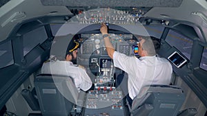 Two pilots are sitting in an airplane cabin and discussing something