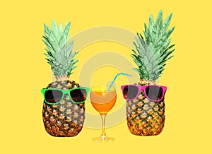 Two pineapple with sunglasses and glass fruit juice on yellow background