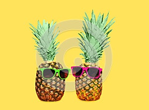 Two pineapple with sunglasses on yellow background, colorful ananas