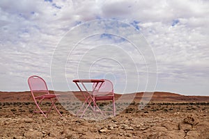 Two pink chairs and one table stand in the Namib desert against the backdrop of a cloudy sky