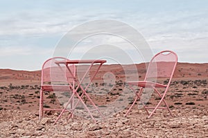 Two pink chairs and one table stand in the Namib desert against the backdrop of a cloudy sky