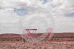 Two pink chairs and one table stand in the Namib desert against the backdrop of a cloudy sky