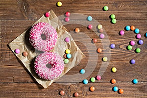 Two pink donuts and colored smarties on wooden table, top view