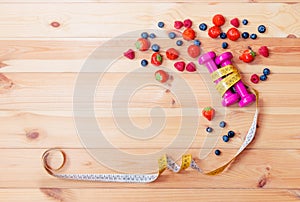 Two pink dumbbells, measuring tape and berries on wooden background