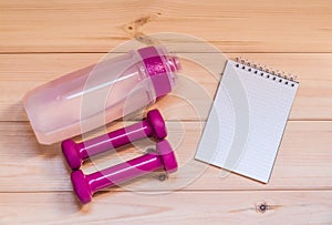 Two pink dumbells, notebook and water bottle