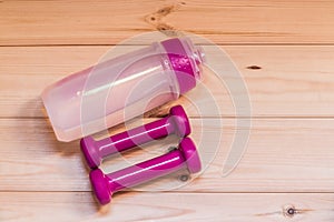 Two pink dumbells and water bottle on wooden background.