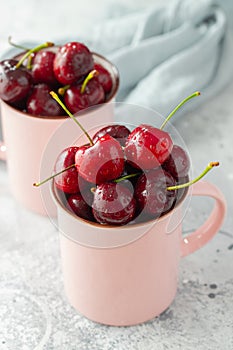 Two pink mugs with fresh ripe cherries. Sweet organic berries on a light concrete background