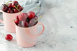 Two pink mugs with fresh ripe cherries. Sweet organic berries on a light concrete background. With copy space