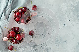 Two pink mugs with fresh ripe cherries. Sweet organic berries on a light concrete background. Top view with copy space