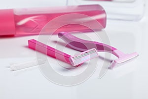 Two pink razor on white table front of a shower gel