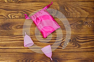 Two pink reusable silicone menstrual cups and silk bag on wooden background. Top view. Concept of feminine hygiene, gynecology