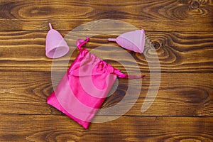 Two pink reusable silicone menstrual cups and silk bag on wooden background. Top view. Concept of feminine hygiene, gynecology