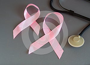 Two pink ribbon awareness breast cancer stethoscope on gray background