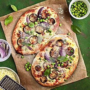 Two pizzas with eggplant, green peas and red onion, top view