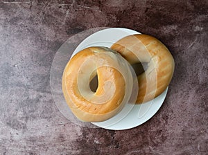 Two plain bagels on a white plate atop a red mottled countertop top view