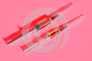 Two plastic disposable syringes with red medicine on a pink back