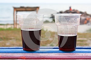 Two plastic glassof wine stands on the colored bench, the sea an