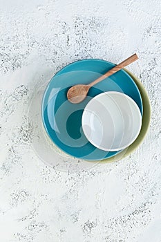 Two plates, a bowl and a wooden spoon on a light gray textural background