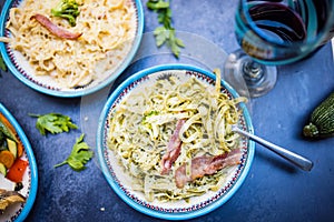 Two plates of delicious pasta with bacon strips above dark surface