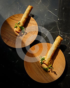 Two plates of food with spring roll, vegetables and sauce on wooden plate